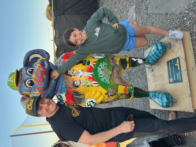 Travis and his daughter, Elinor, pose with a statue of Stomper, the mascot for the Oakland A's.