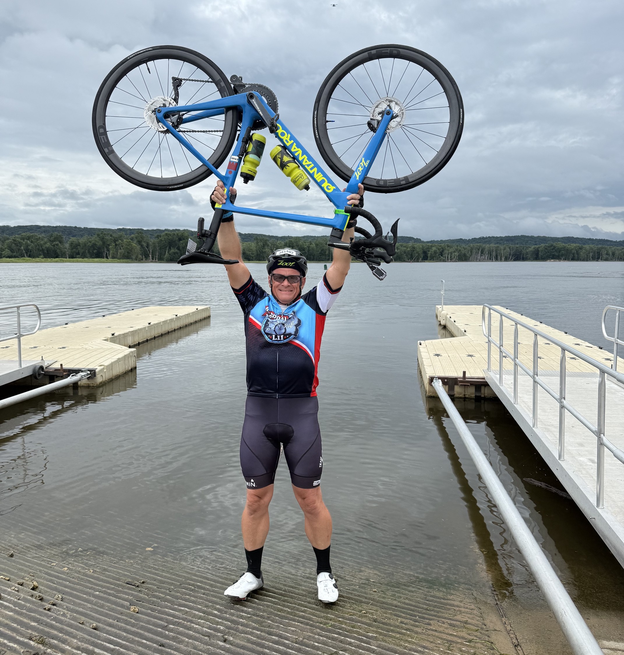 Brian raises his bicycle in triumph on the bank of the Mississippi River after completing the RAGBRAI, an annual seven-day bicycle ride across the state of Iowa.